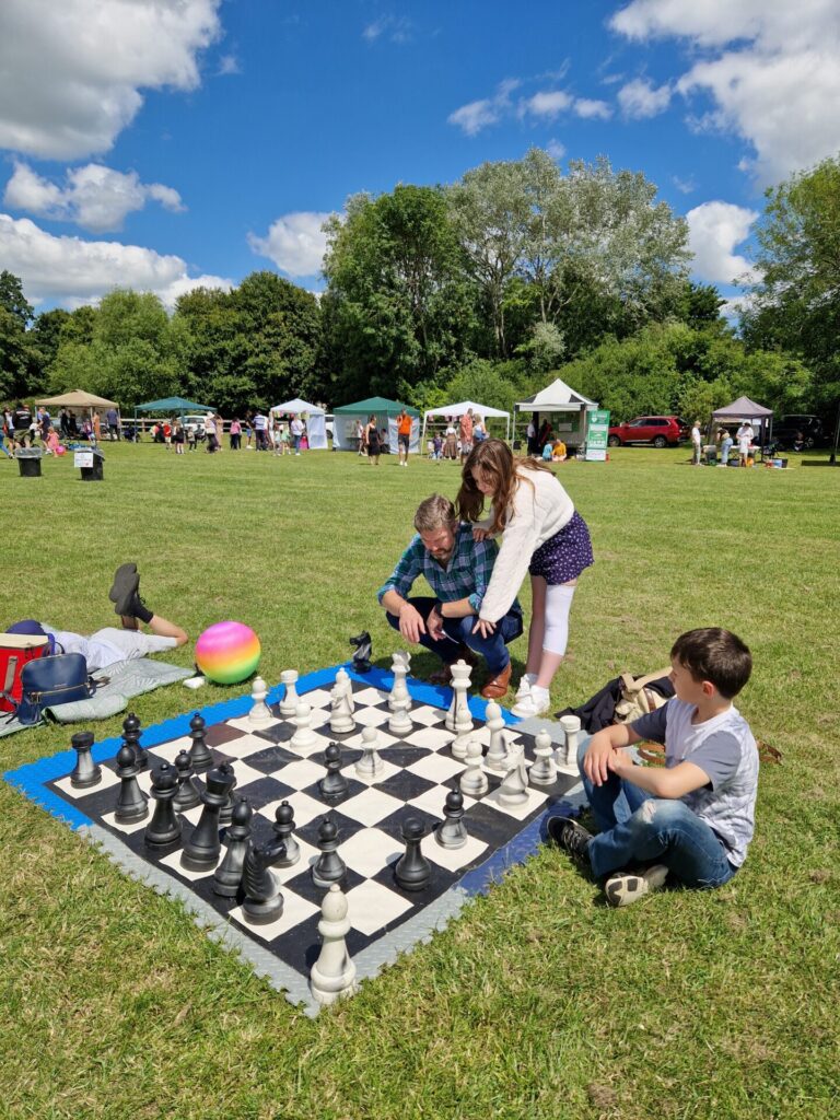 Image shows a family playing a giant chess game in a paddock at a community event