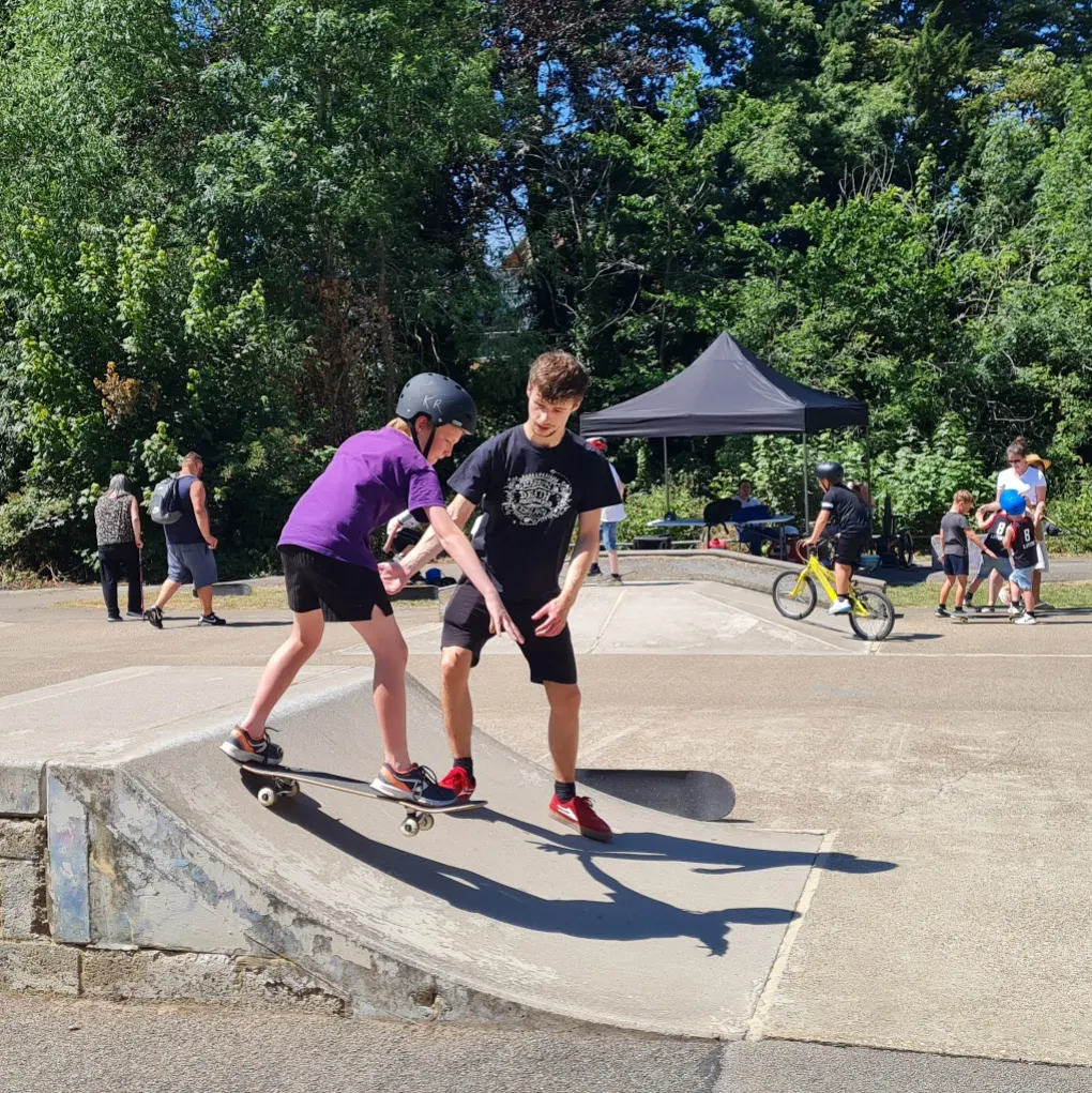 Image shows a young skateboarder on the ramps being couched by a professional skateboarder.